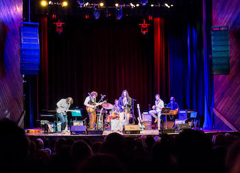 A band performing with guitars, bass, and drums on stage at the Berklee Performance Center.