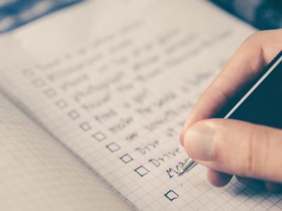 Close up of hand holding a pen making a checklist on grid notebook paper