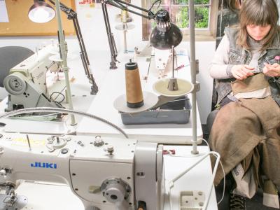 Person hand-sewing a garment in a sewing studio with sewing machines