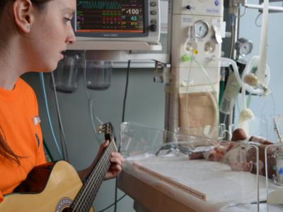 Young woman playing guitar to a newborn baby in the hospital