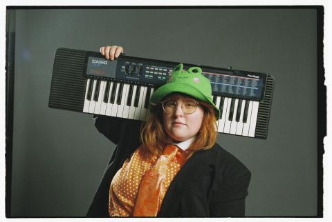 corook wearing a frog hat, holding a keyboard on their shoulder