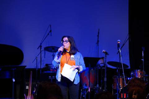 A woman, short dark hair, speaking into a microphone.